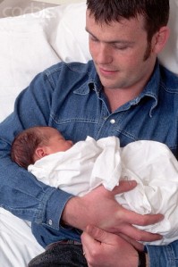 Father Cradling Newborn Baby In Hospital